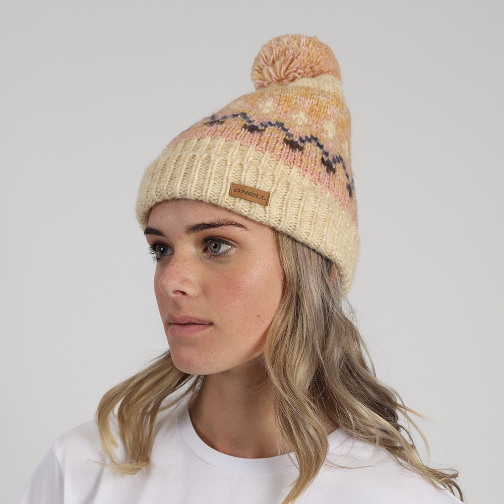 Woman wearing a patterned knit beanie with a pom-pom on a plain background