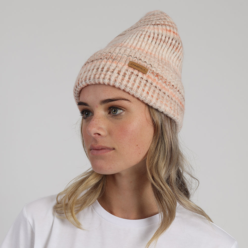 Woman wearing a beige knit beanie with a brand logo on a light gray background