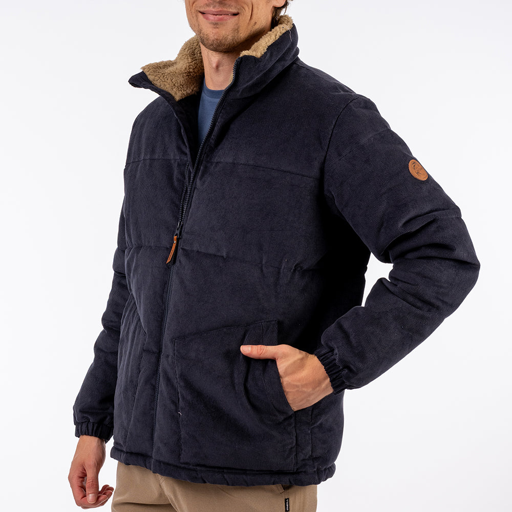 Man wearing a dark blue jacket with brown collar and patch on a white background