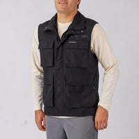 Man wearing a black vest with multiple pockets on a plain background