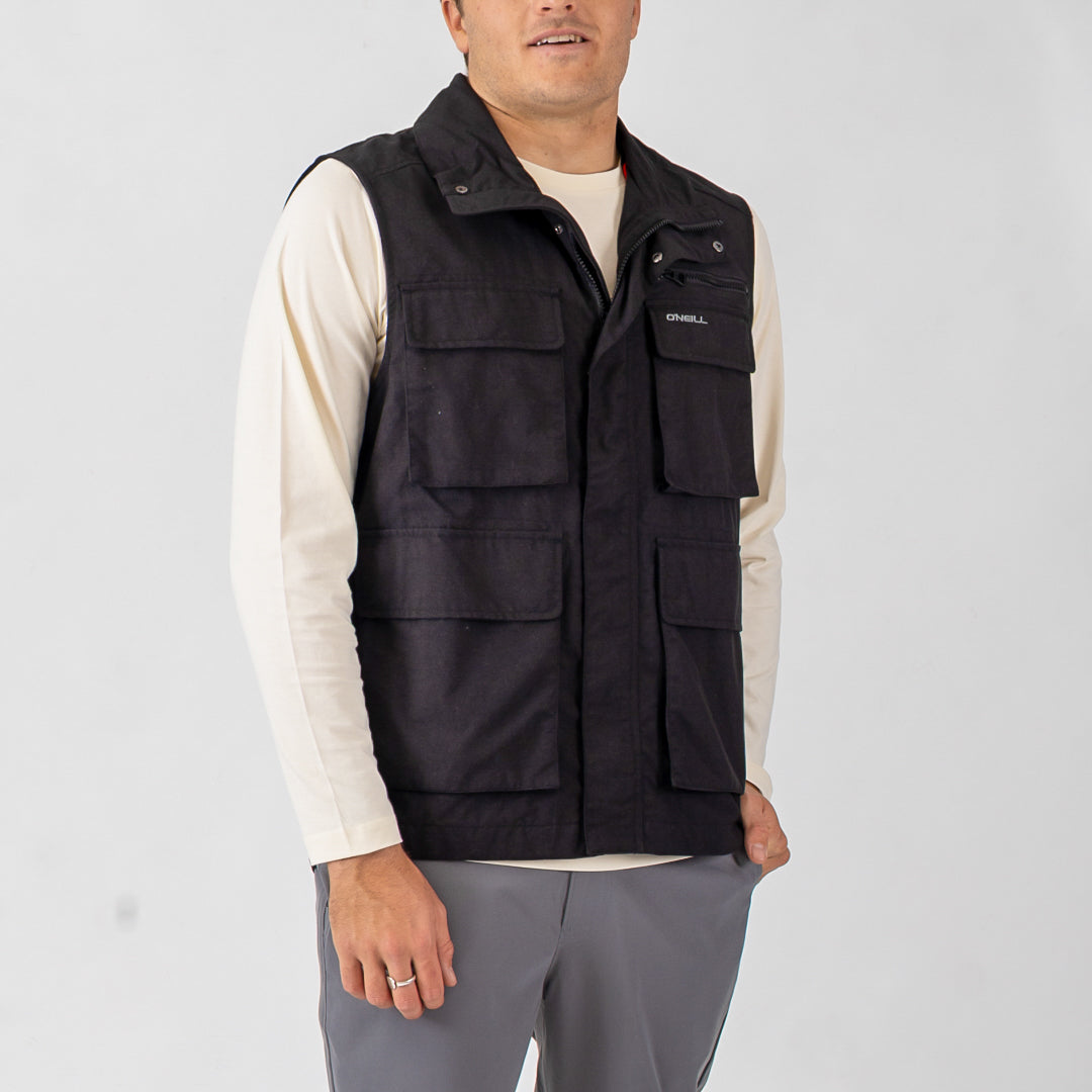 Man wearing a black vest over a white shirt on a light gray background