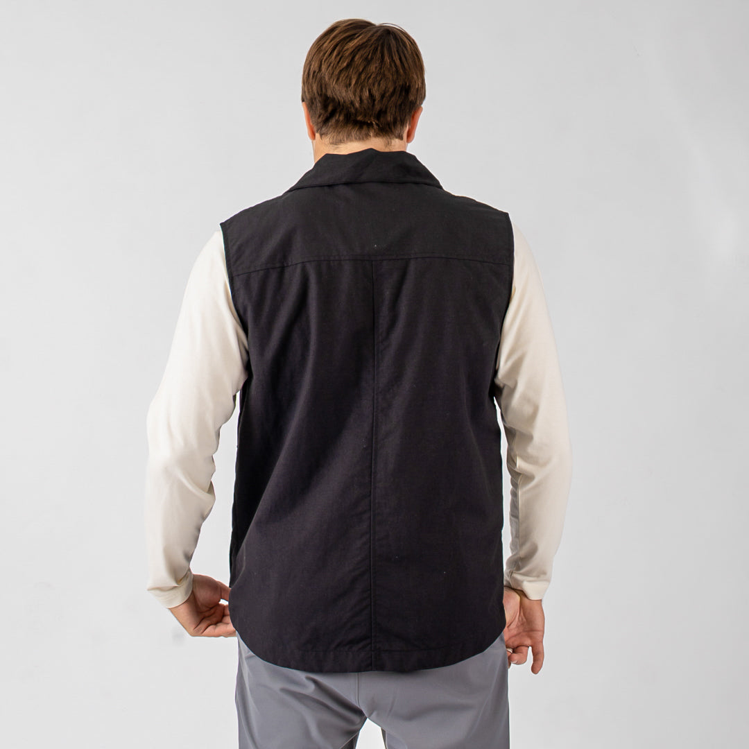 Person wearing a black vest over a light-colored shirt on a plain background