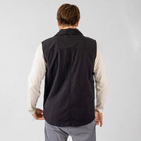 Person wearing a black vest over a light-colored shirt on a plain background