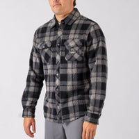 Person wearing a black and gray plaid shirt with a brand logo on a light gray background