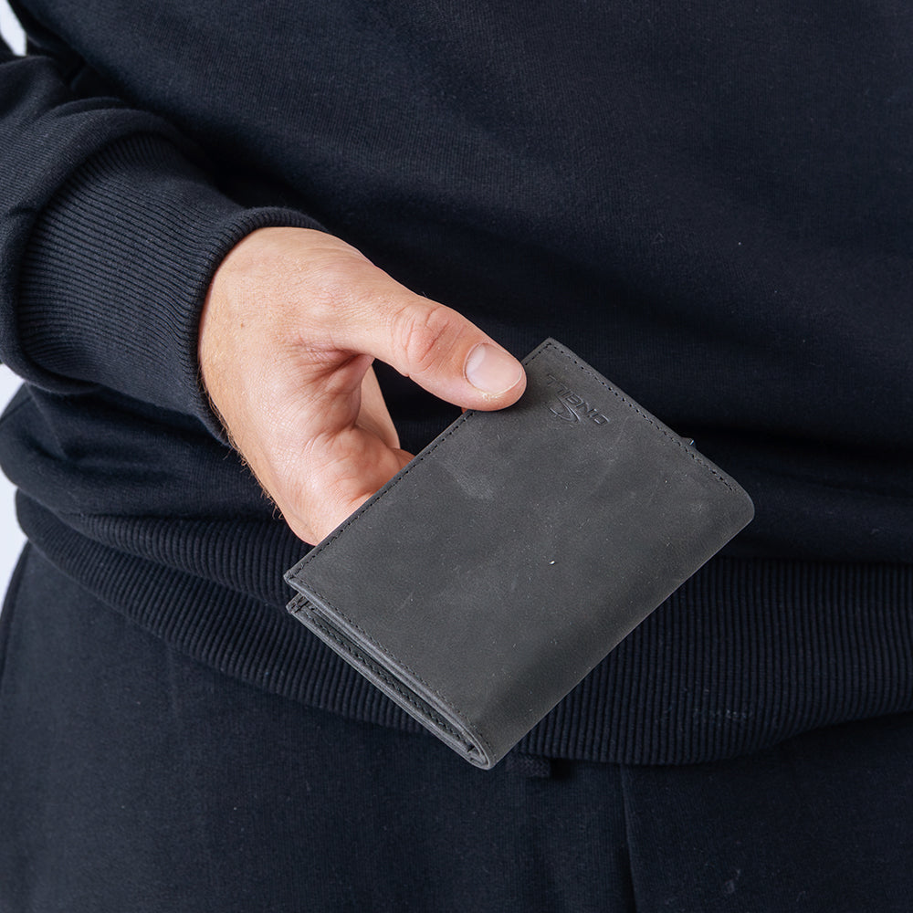 Person holding a black leather wallet against a dark background