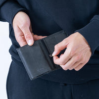 Person holding a black leather wallet with a visible brand name.