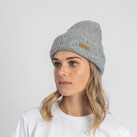 Person wearing a gray knit beanie with a brand logo on a white background