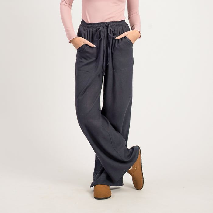 Person wearing dark gray wide-leg pants with a light pink top on a white background
