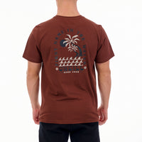 Brown t-shirt with a palm tree design on the back, worn by a person.