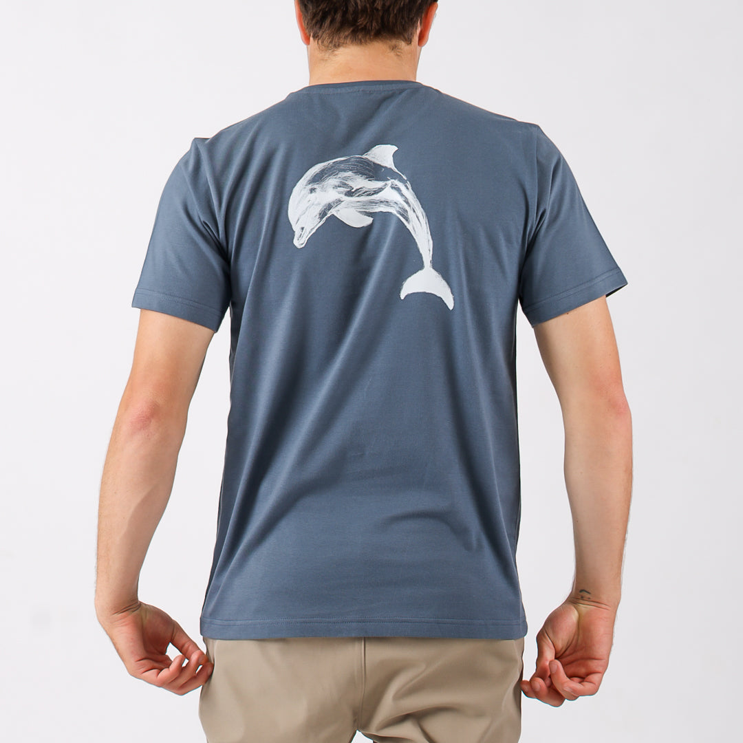 Person wearing a blue t-shirt with a dolphin design on the back against a light gray background