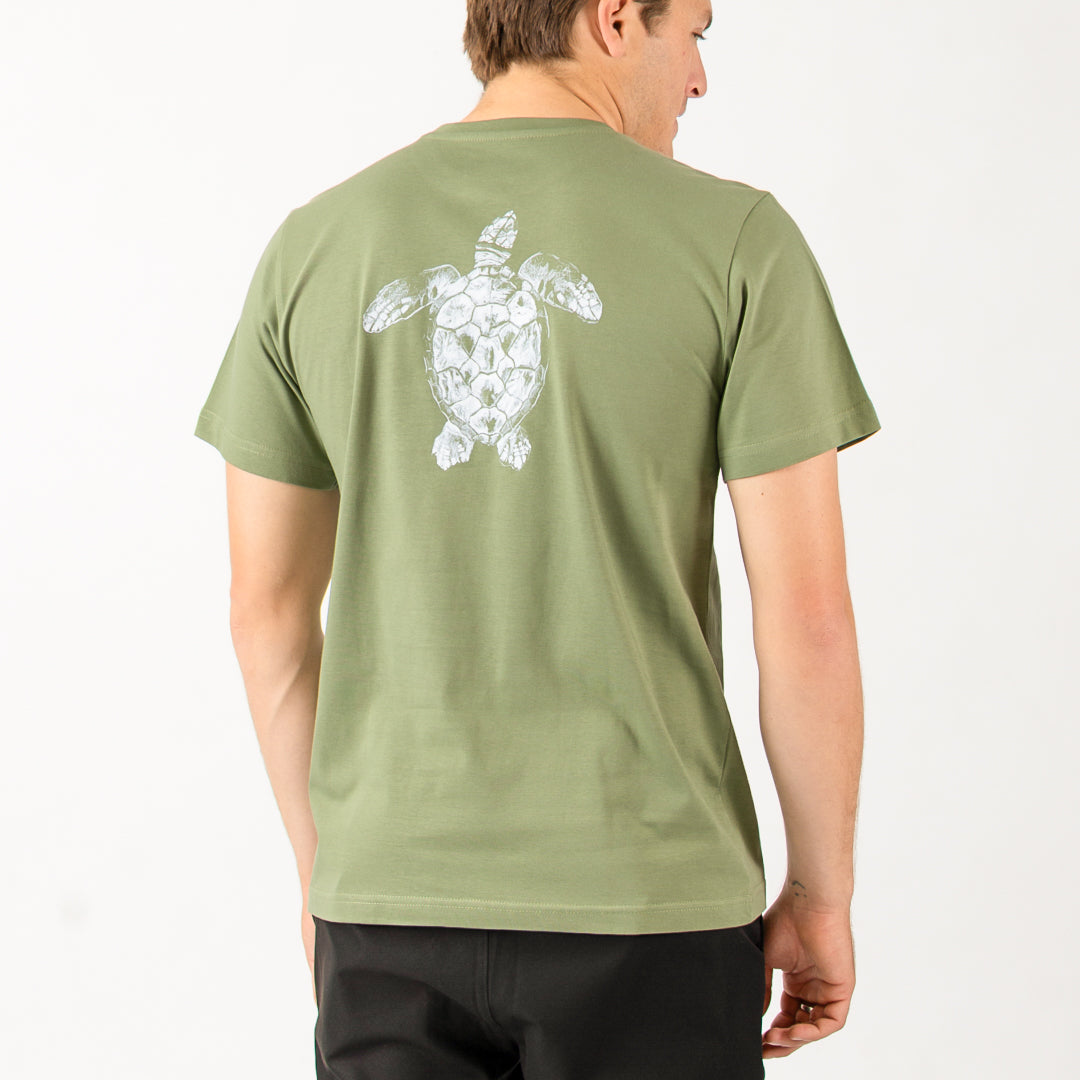 Person wearing a green t-shirt with a turtle design on the back, standing against a white background