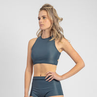 Woman wearing a dark green sports bra and shorts set on a light gray background